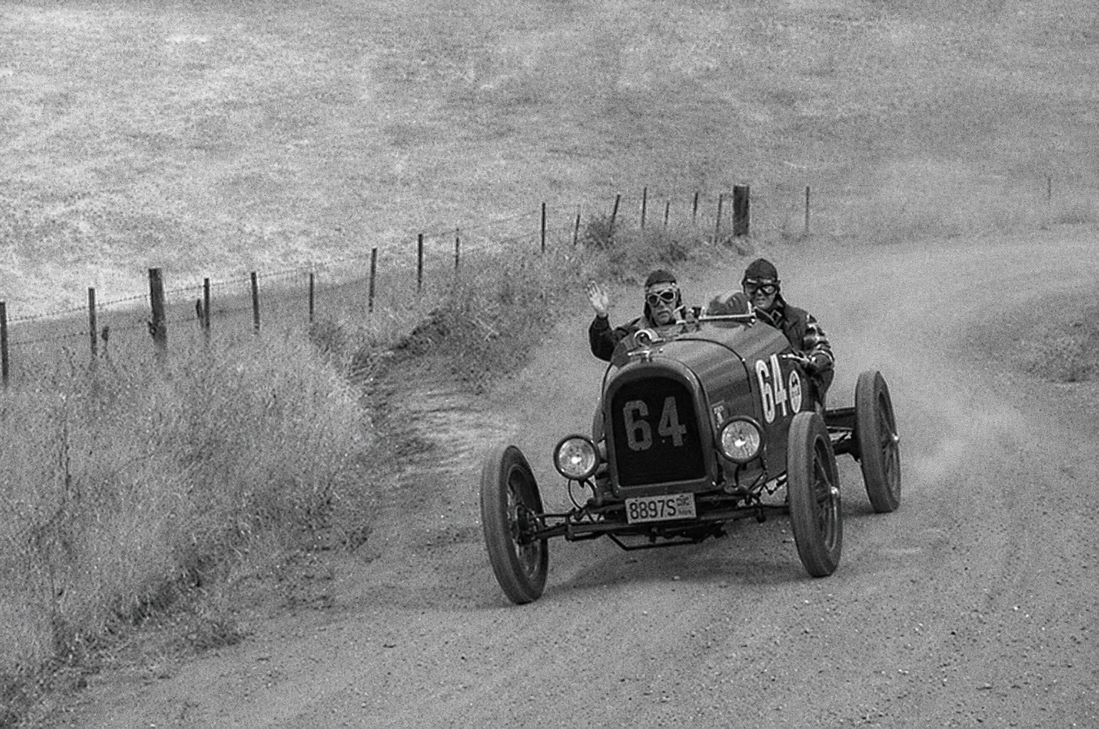 A vintage No. 64 race car kicking up dust on a dirt road.